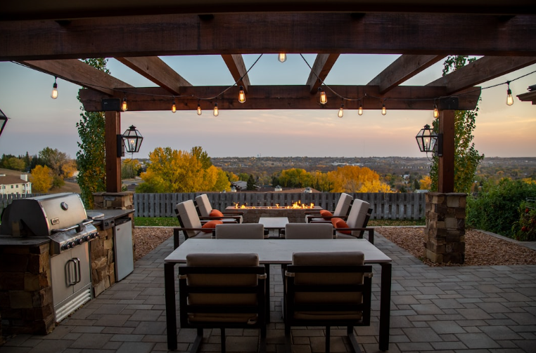 Covered outdoor dining pergola in Fort Worth TX with string lights, firepit, and grill, demonstrating weatherproof design features for year-round use.
