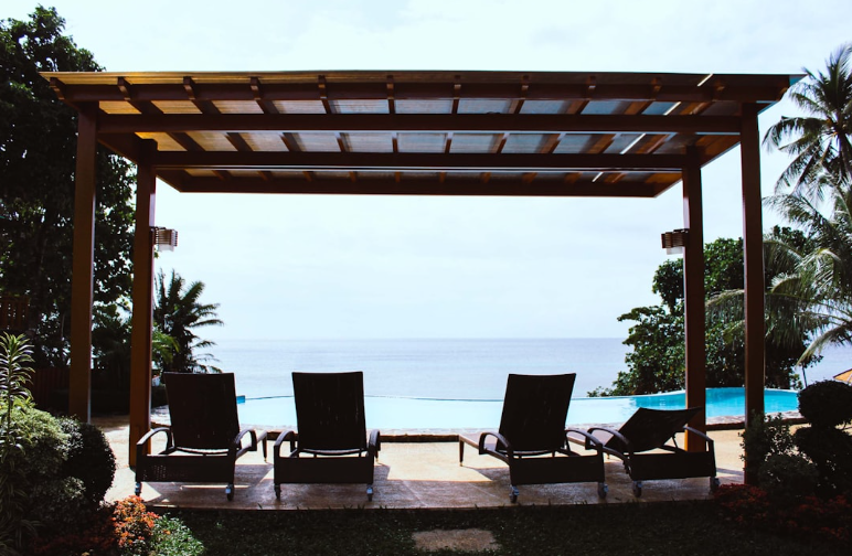 Poolside wooden pergola with lounge chairs overlooking the ocean, representing pergola care and maintenance for durability in Fort Worth TX.
