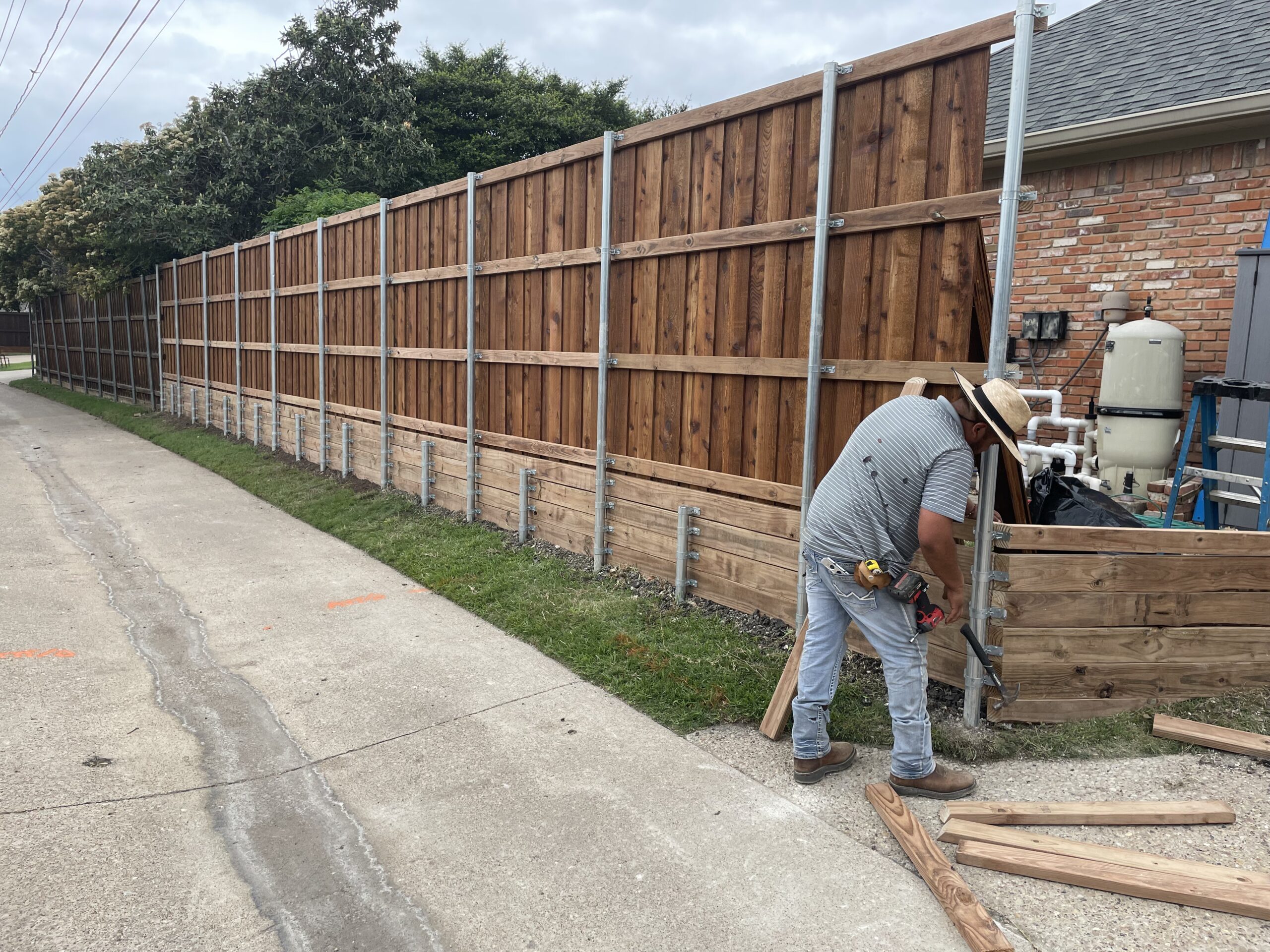 worker installs a wooden and metal fence along an alley, showcasing sustainable wood and cedar materials for landscaping projects.