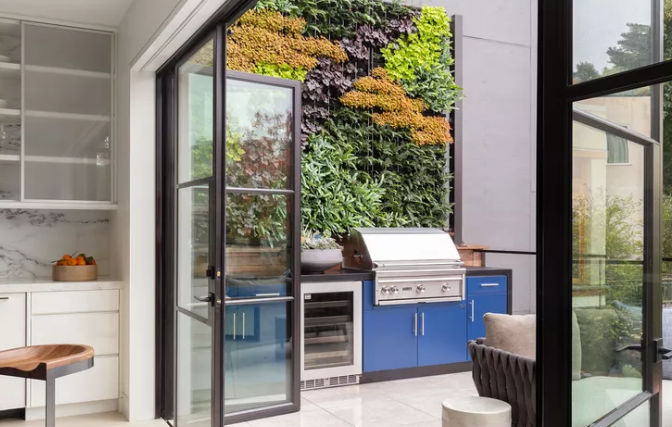 Modern outdoor kitchen with blue cabinetry and vertical garden integrated into patio landscape.