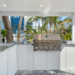 outdoor kitchen with stainless steel grill and white cabinetry under a modern pergola.