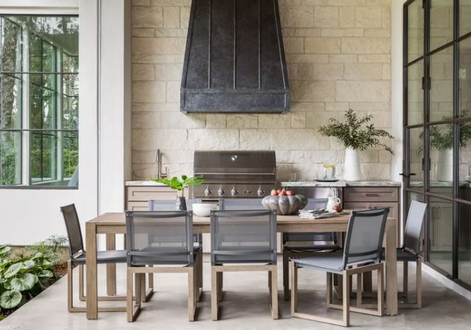 Modern custom outdoor kitchen and dining area in Fort Worth with built-in grill, stone wall, and sleek patio furniture.