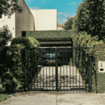 Black wrought iron driveway gate with greenery enhancing home security and curb appeal.
