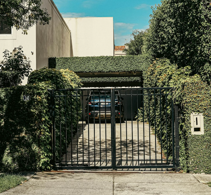 Black wrought iron driveway gate with greenery enhancing home security and curb appeal.