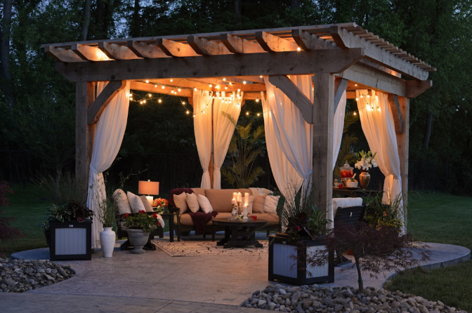 Rustic wooden pergola with draped curtains, string lights, and cozy seating area at dusk.